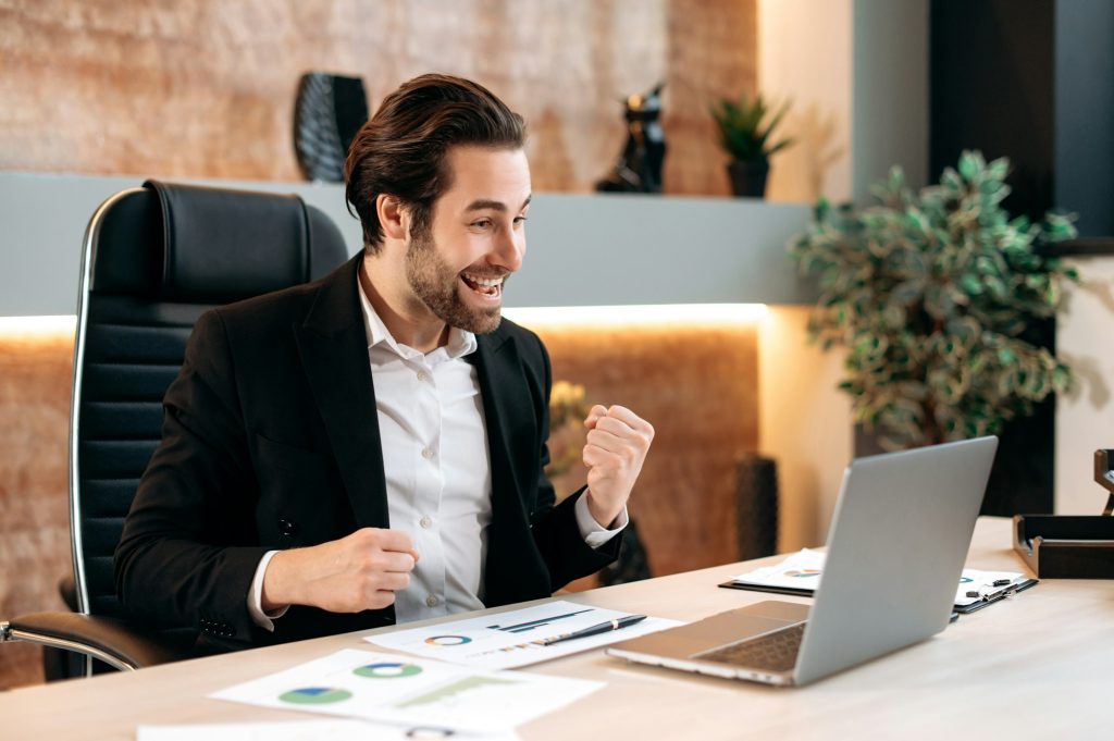 Big profit, success. Happy cheerful caucasian businessman, office worker, sits at a workplace in